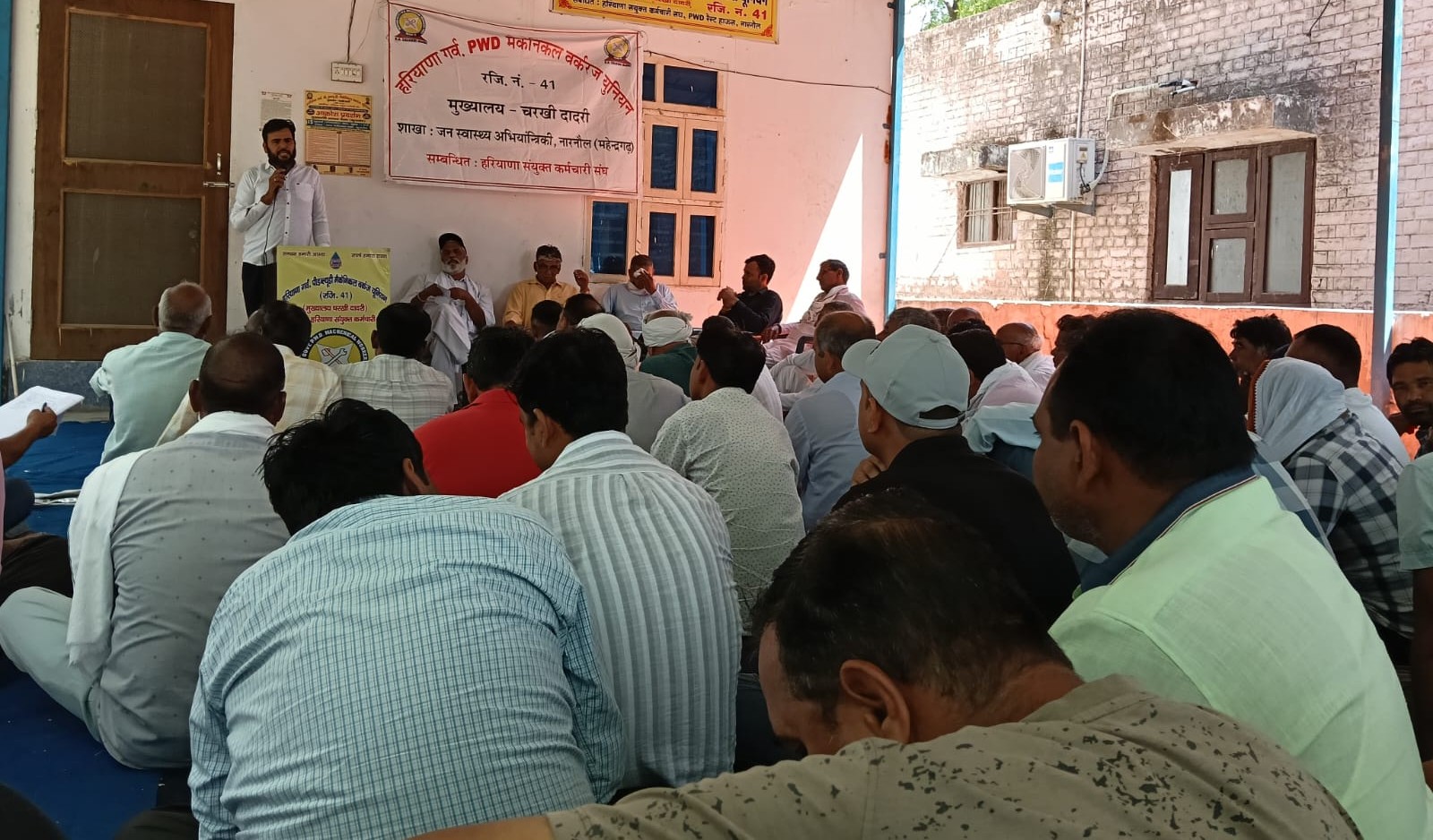 बैठक के दौरान मंच पर मौजूद पदाधिकारी और सामने बैठे कर्मचारी, समस्याओं को लेकर गंभीर चर्चा।